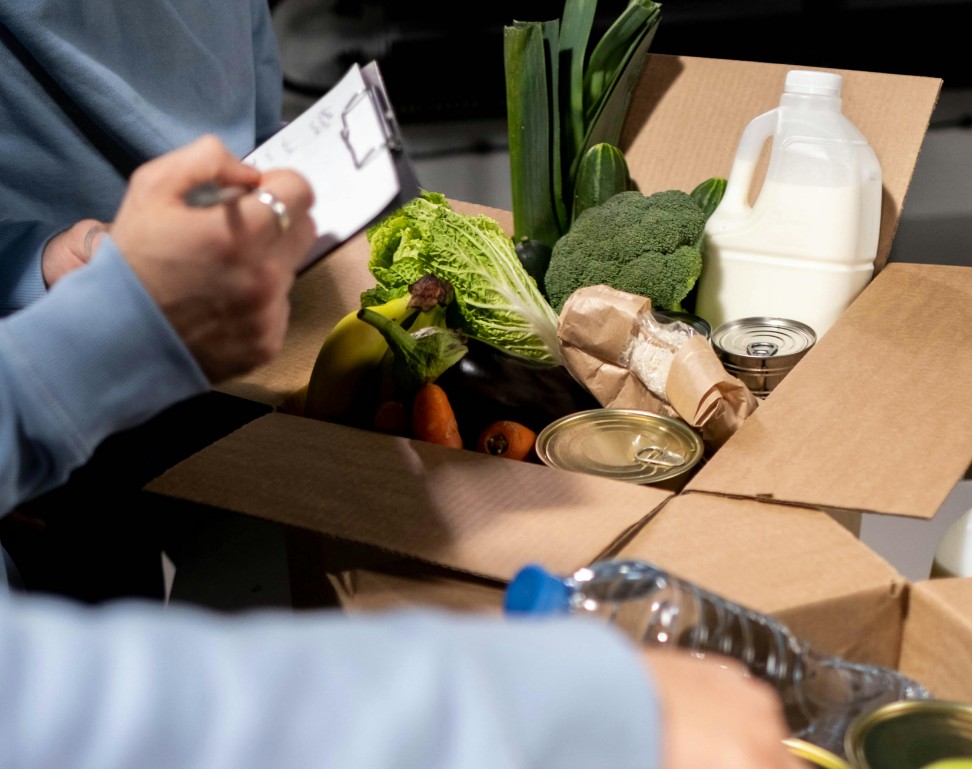 A hand hold a checklist while reviewing a box of produce.