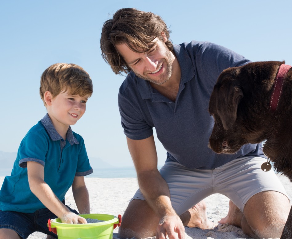Father and son with family dog, playing in the sand.